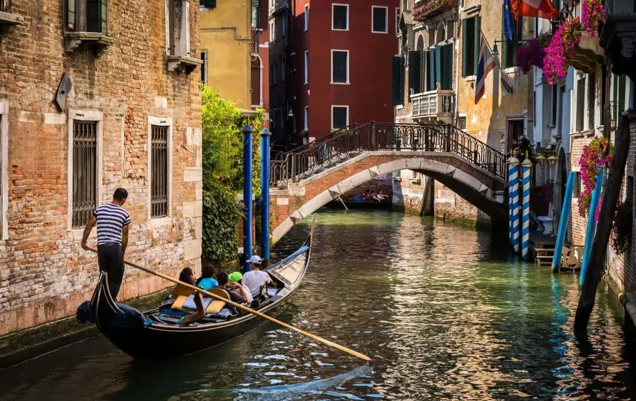 Gondola in un canale veneziano, tra palazzi antichi e fiori colorati. Scopri gli angoli nascosti di Venezia.