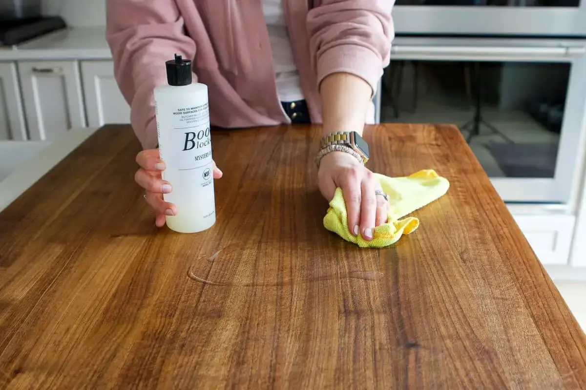 A person demonstrates how to clean butcher block countertops using a cleaning solution and a yellow cloth.