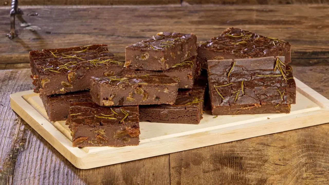 Fette di castagnaccio lucchese, dolci scuri con rosmarino e uvetta, disposti su un tagliere di legno.