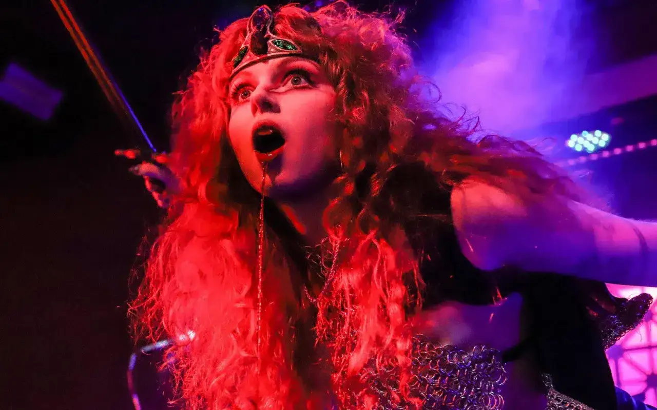 Eine Frau mit roten Locken und einem Diadem, die wie eine Kriegerin der Metal-Szene aussieht, singt mit weit geöffnetem Mund.