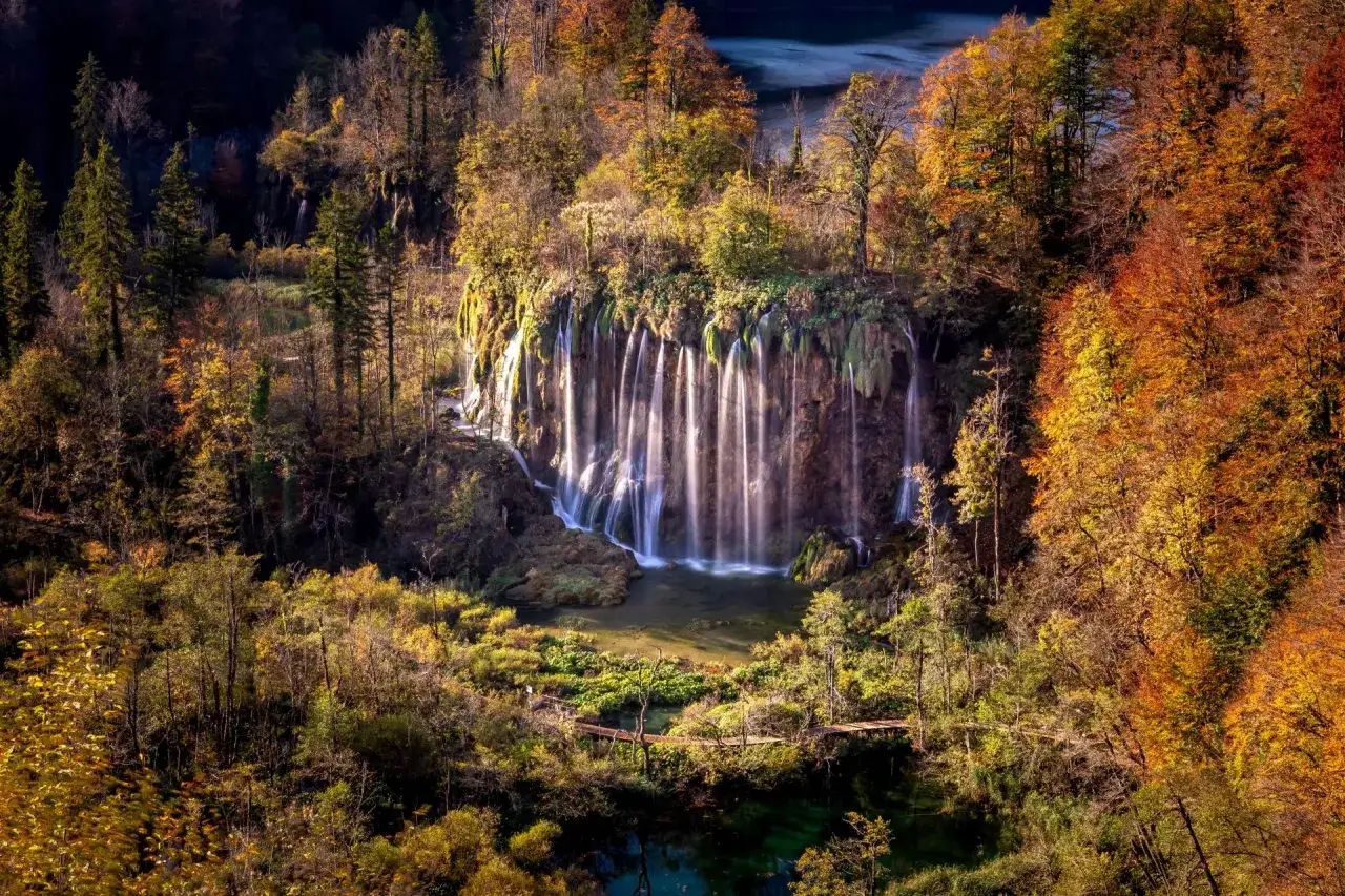 Herbstlicher Wasserfall in Kroatien im Oktober, umgeben von leuchtenden Farben. Das Wetter ist mild, ideal für Spaziergänge auf Holzstegen.