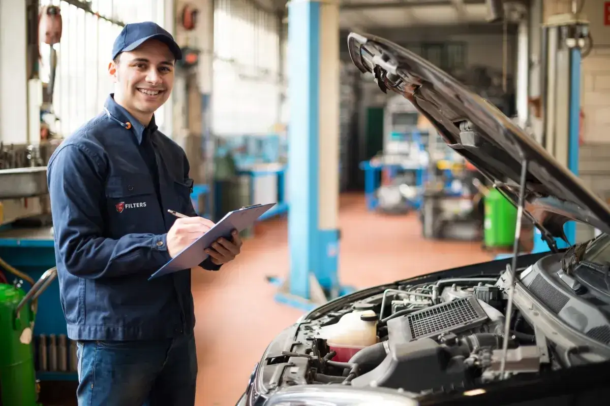 Mechanik z notatkami przy samochodzie z otwartą maską. Zastanawia się, co ile wymieniać olej 5w30, by silnik działał sprawnie.