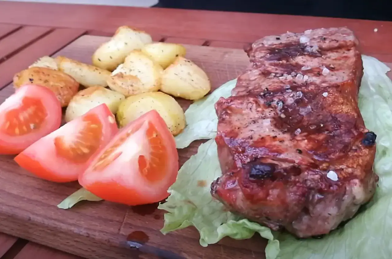 Pyszny stek z grilla, podany z pieczonymi ziemniaczkami i pomidorami na drewnianej desce.