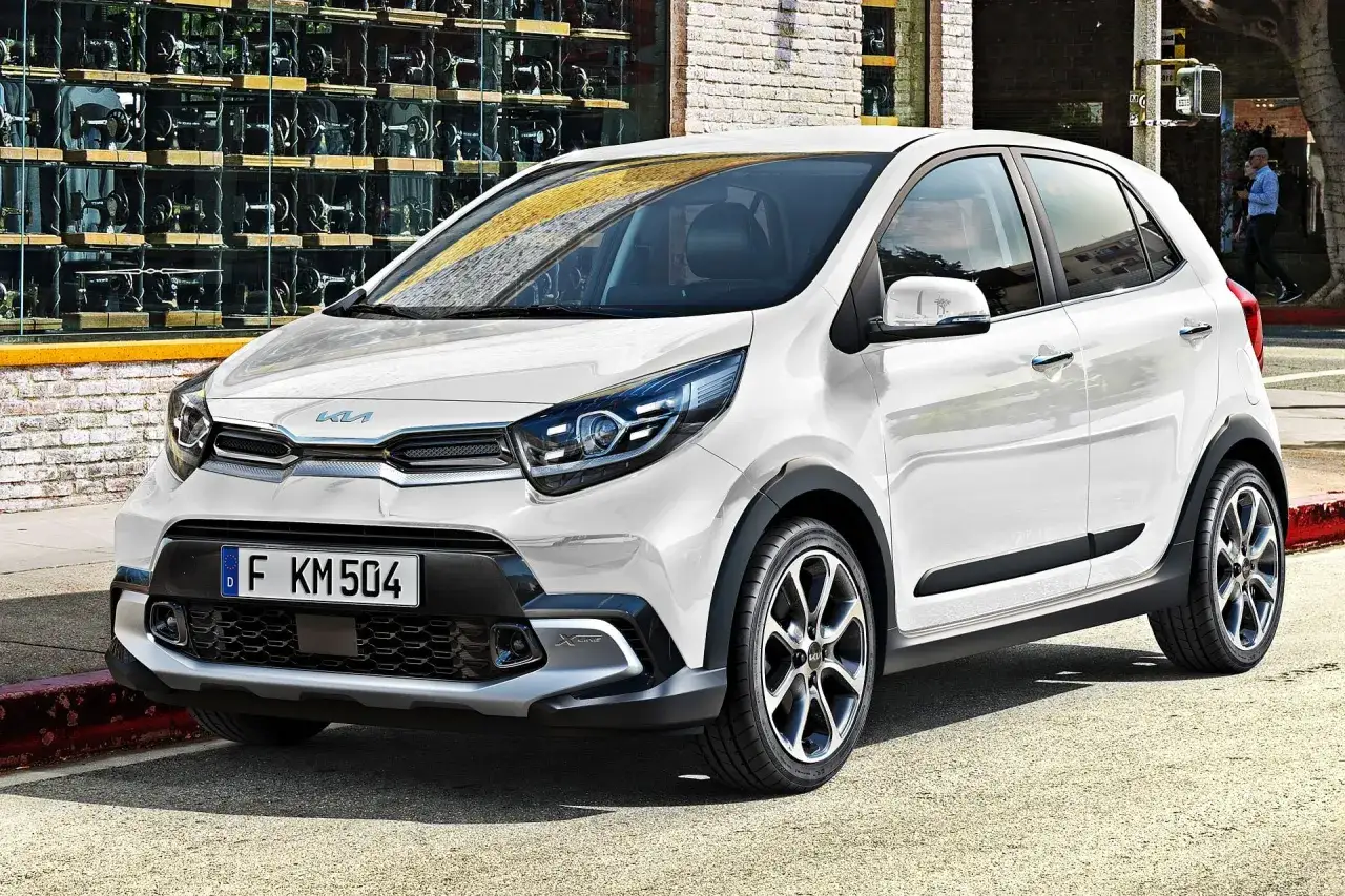 Biały Kia Picanto X-Line, jeden z popularnych kia modele, parkuje na ulicy przed budynkiem z witryną pełną maszyn do szycia.