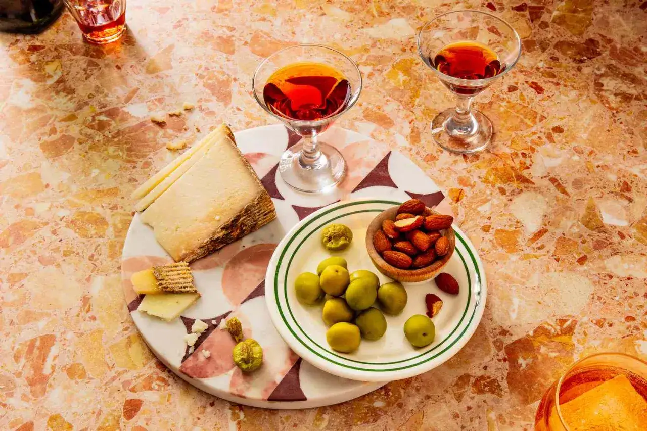Aperitif co to? Dwa kieliszki czerwonego drinka, ser, oliwki, migdały i suszone figi na marmurowym blacie. Idealne na początek wieczoru.