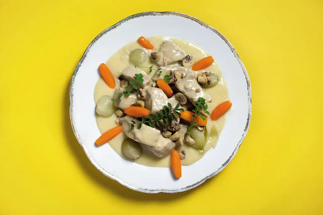 Une assiette de blanquette de veau, garnie de carottes, d'oignons grelots et de champignons, nappée d'une sauce onctueuse.