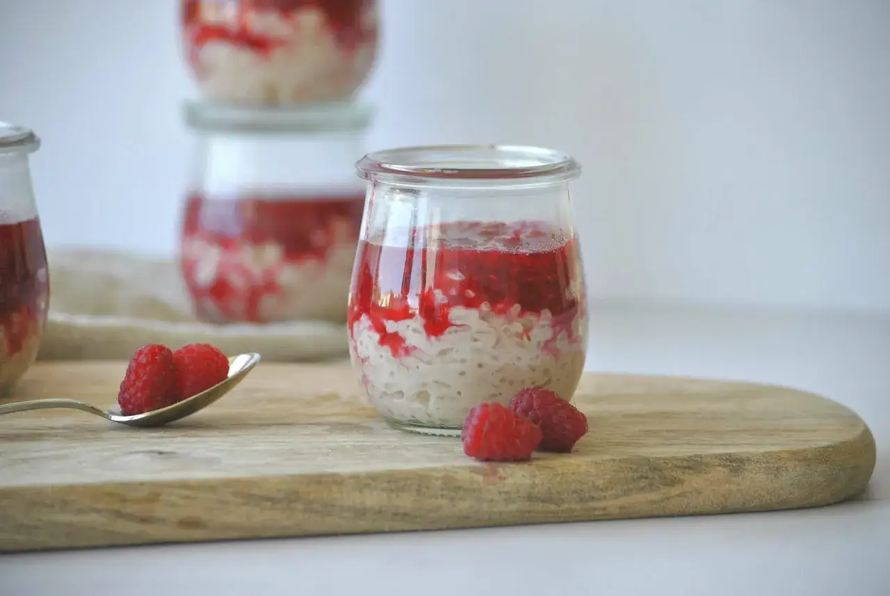 Milchreis einkochen in Gl&auml;sern mit Himbeerso&szlig;e. Frische Himbeeren auf einem L&ouml;ffel und daneben.