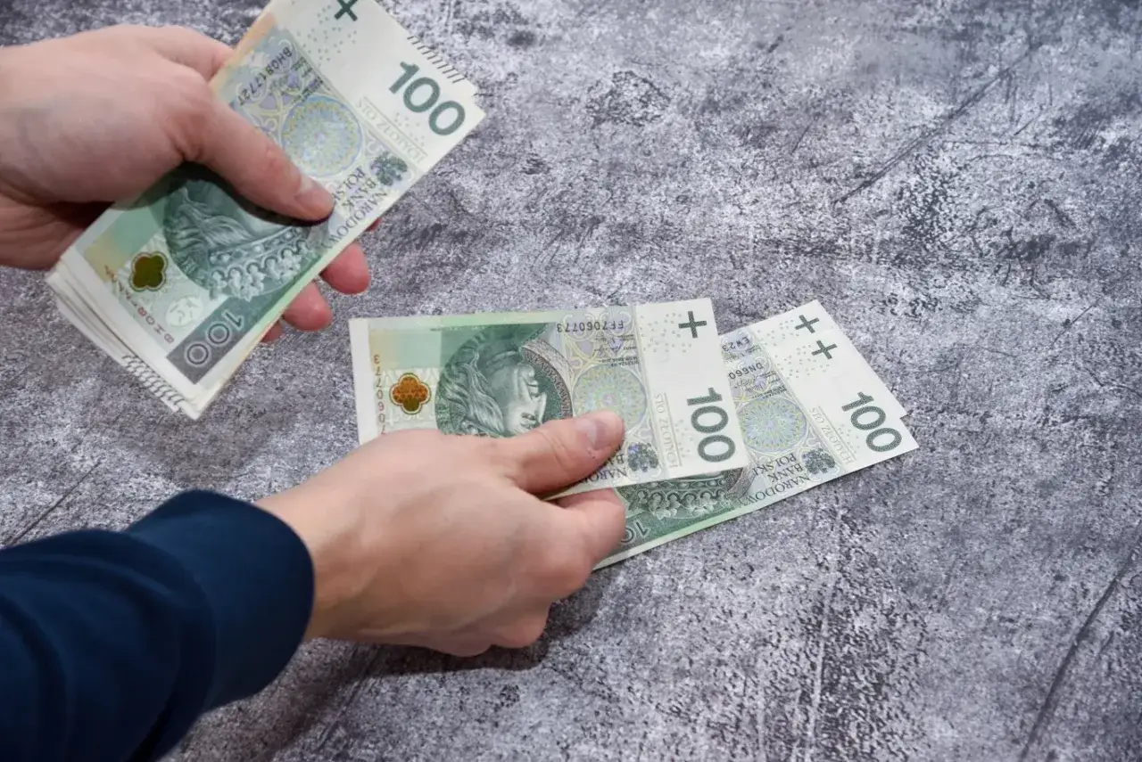 Dwie ręce liczą banknoty 100 zł. Jedna ręka trzyma plik banknotów, druga rozkłada kilka sztuk, zbliżając się do limitu.