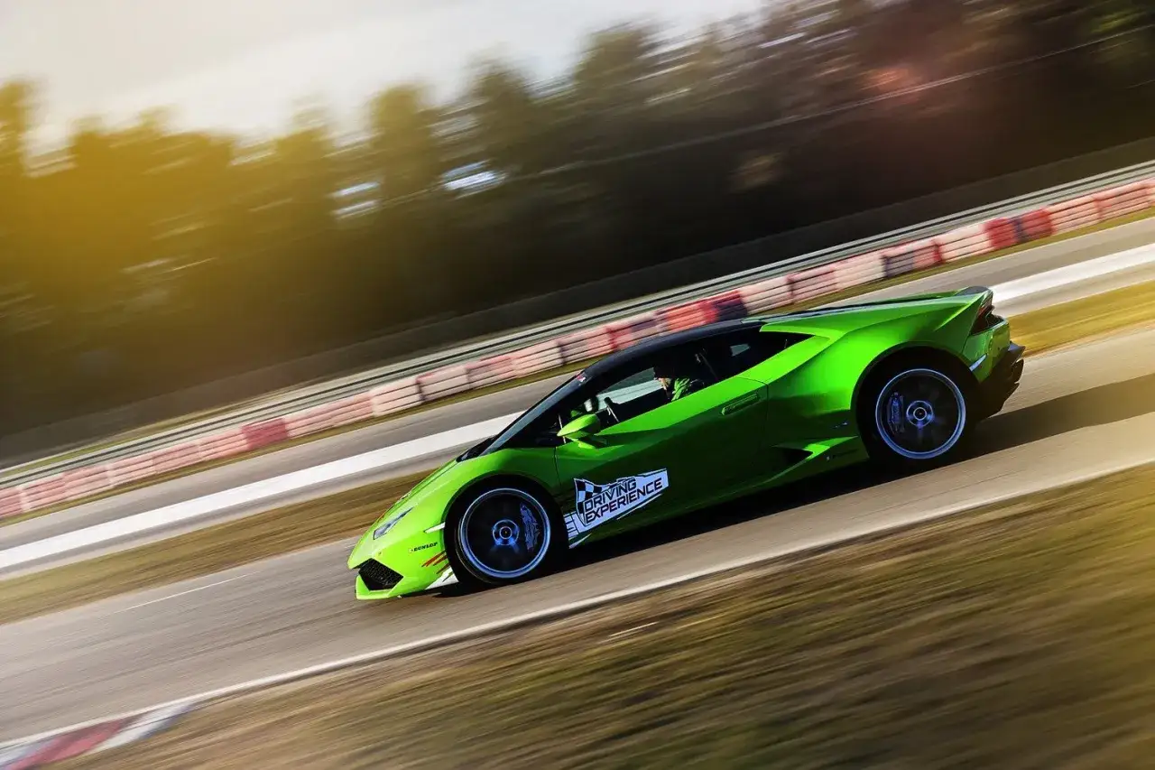 Zielony Lamborghini na torze wyścigowym, w tle rozmyte drzewa i niebo. Ekscytujący przejazd lamborghini po torze.