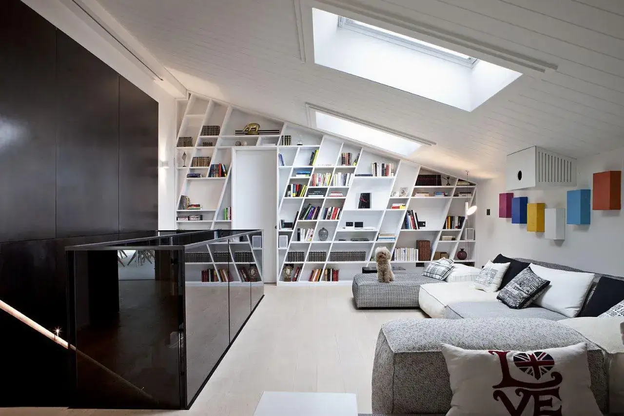 Ristrutturazione mansarda: libreria a parete su misura, divani modulari e lucernari che illuminano l'ambiente.
