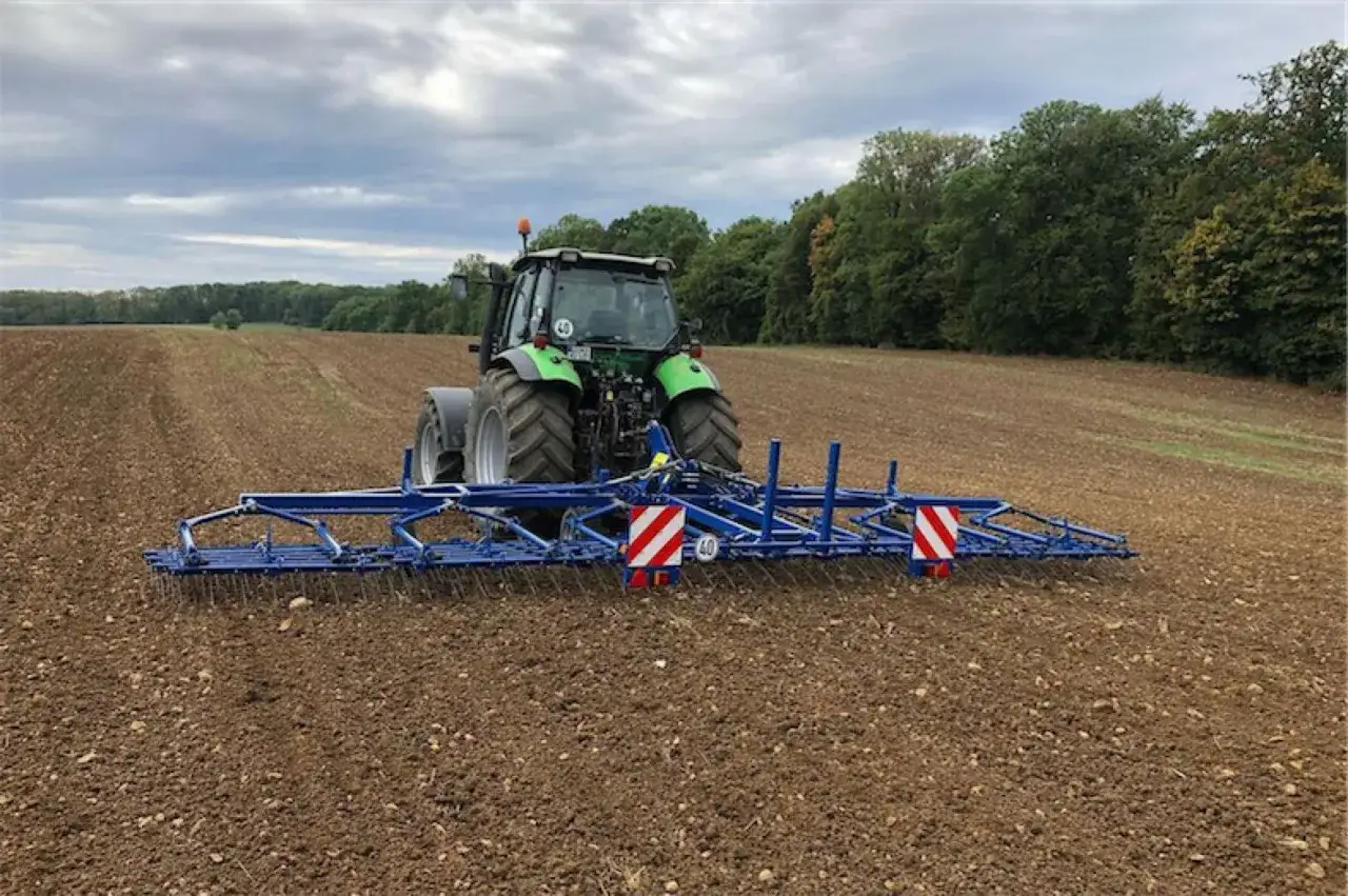 Zielony traktor z broną zębową pracuje na polu, przygotowując ziemię. To skuteczne narzędzie, co na chwasty, które usuwa niechciane rośliny.