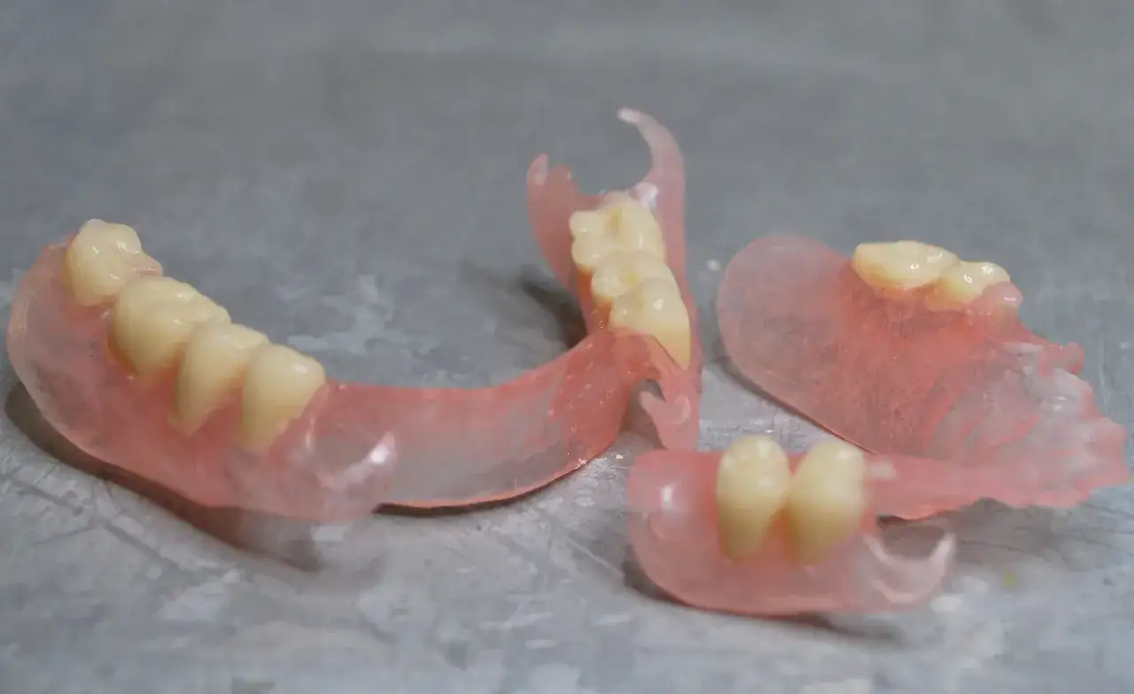 Denti artificiali rosa traslucidi, parte delle ultime generazioni di protesi dentarie mobili invisibili, su una superficie grigia.