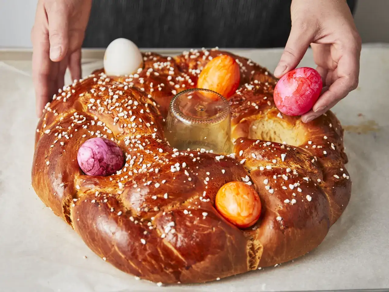 H&auml;nde schm&uuml;cken einen goldbraunen Osterkranz mit bunten Eiern. Das Backen des Osterkranzes ist fast vollendet.