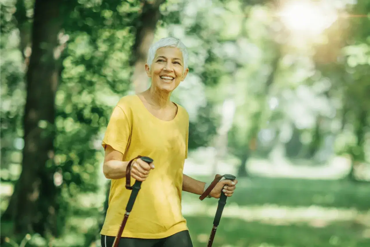 Une femme souriante profite de la vitesse marche nordique dans un parc ensoleill&eacute;.