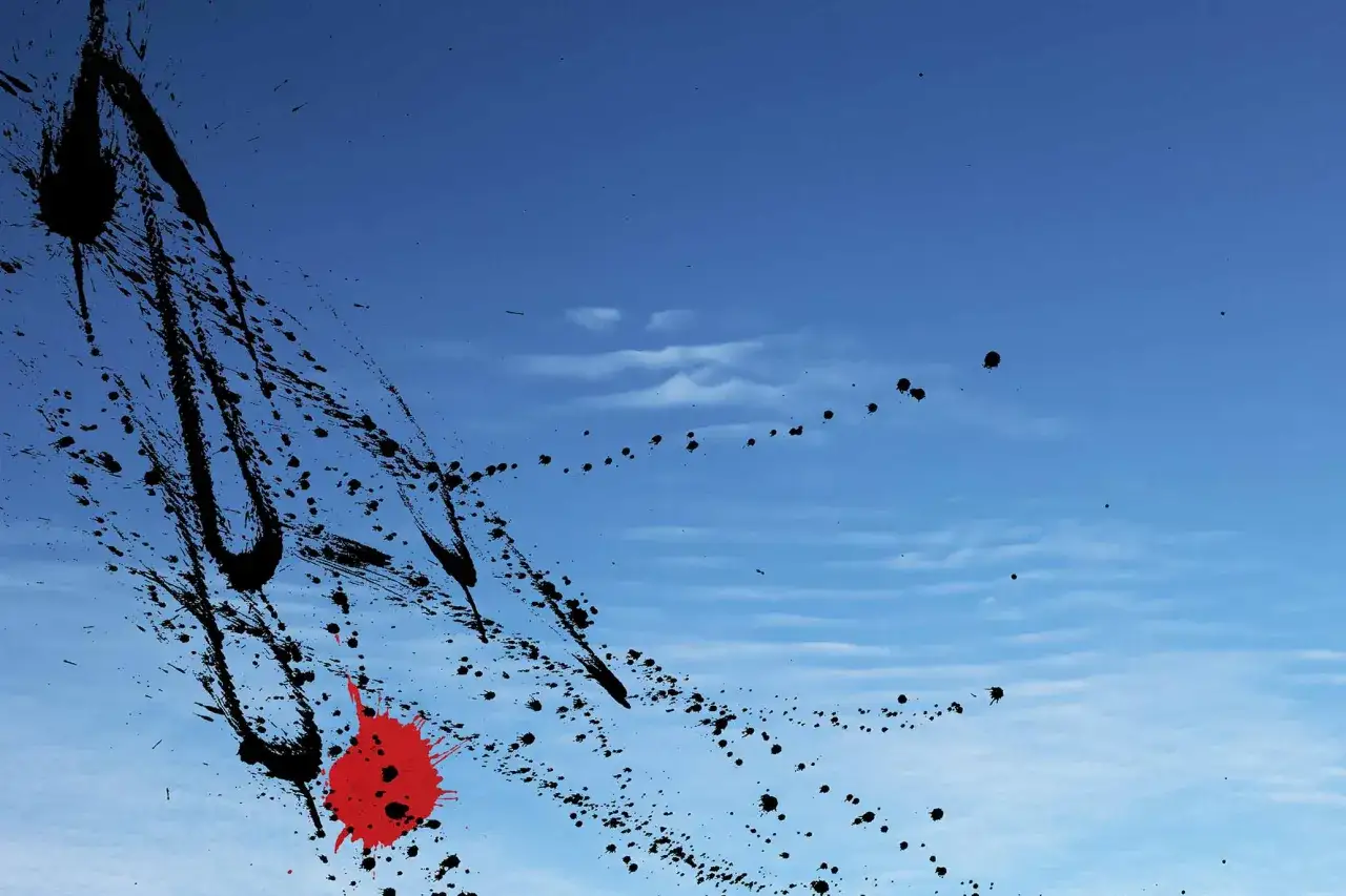 Torben Ulrichs Kunst: Schwarze und rote Farbspritzer auf blauem Himmel, wie ein dynamischer Pinselstrich.