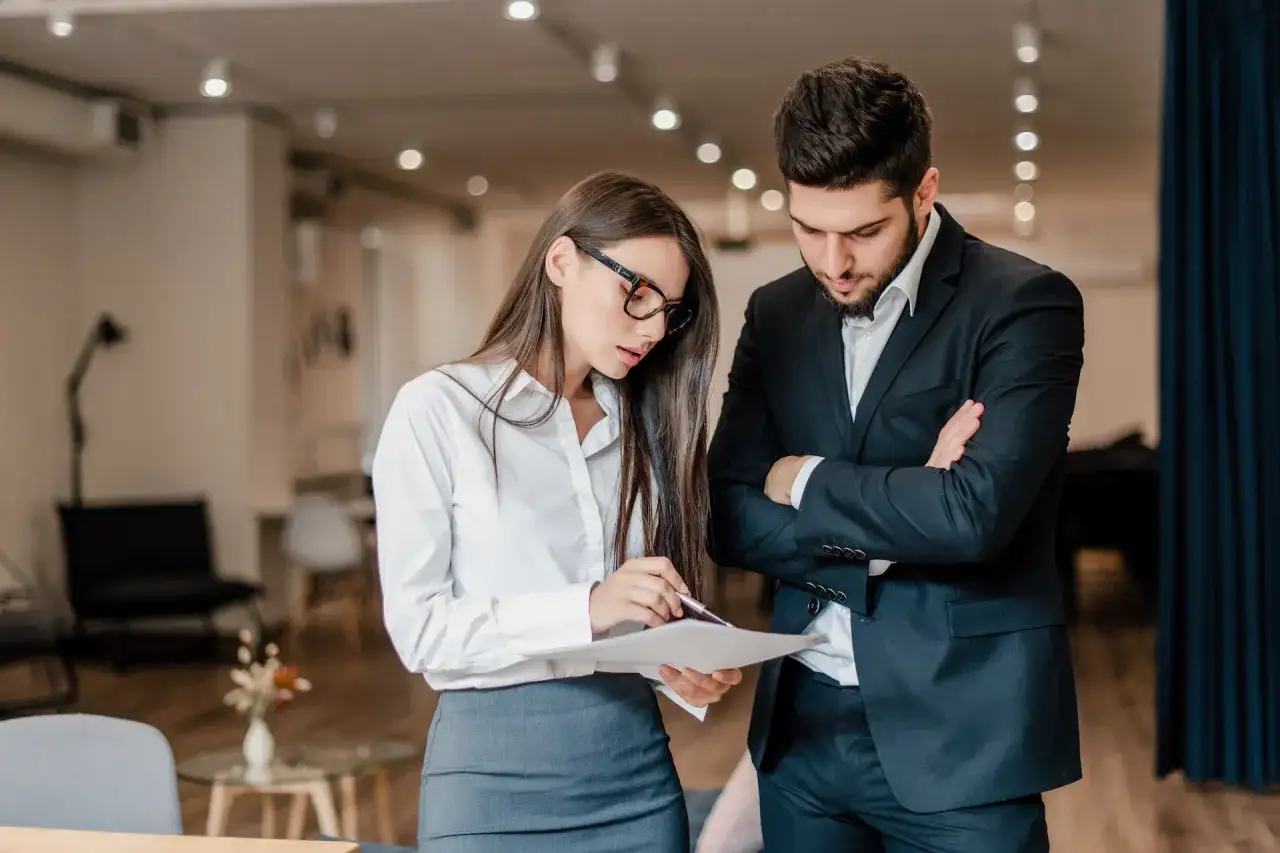 Uomo e donna discutono documenti in ufficio, pianificando un evento. Il loro codice ATECO per l'organizzazione eventi è fondamentale per il successo.