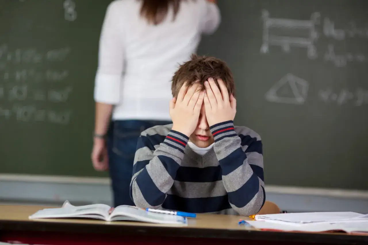 Chłopiec z zespołem Aspergera zakrywa twarz dłońmi, przytłoczony bodźcami w klasie.