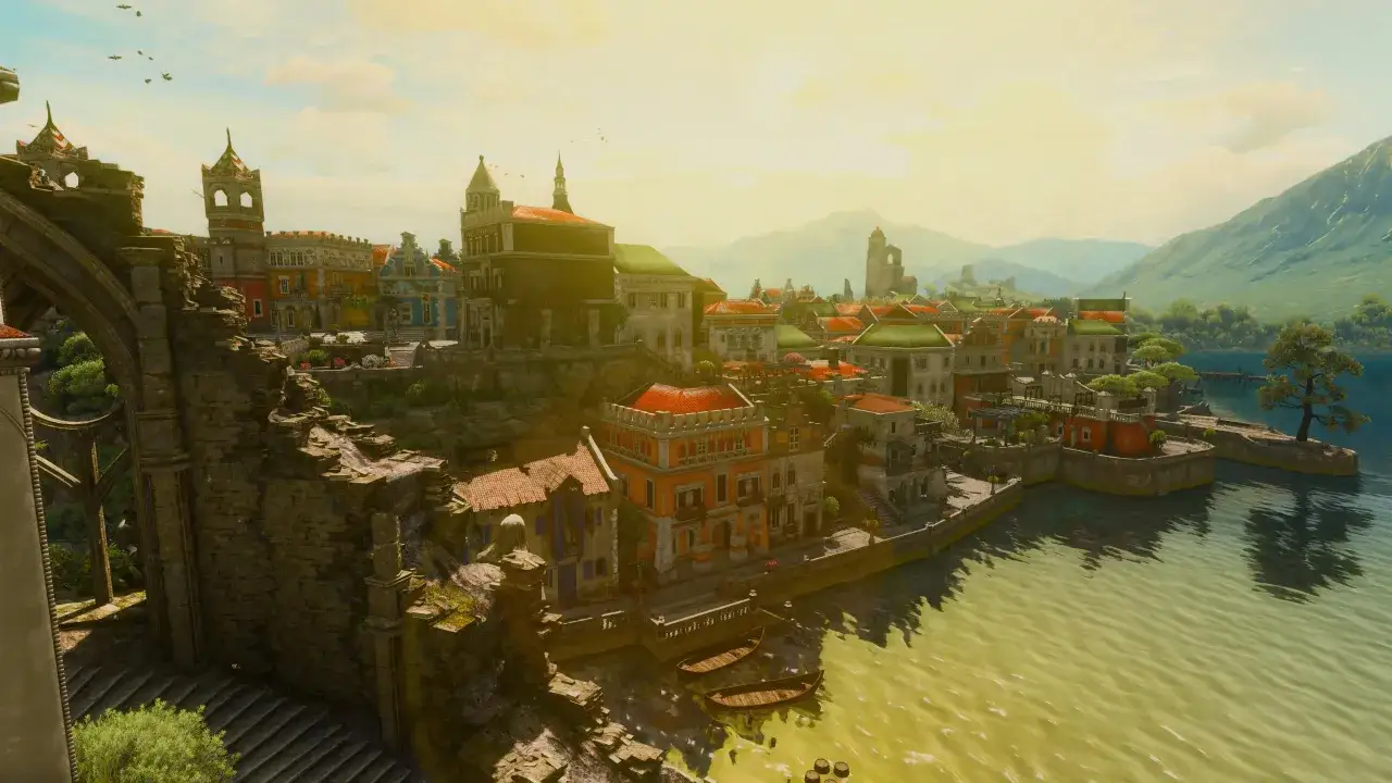 Sonnenbeschienene Stadt am Wasser mit Bergen im Hintergrund, wie in The Witcher 3: Blood and Wine.