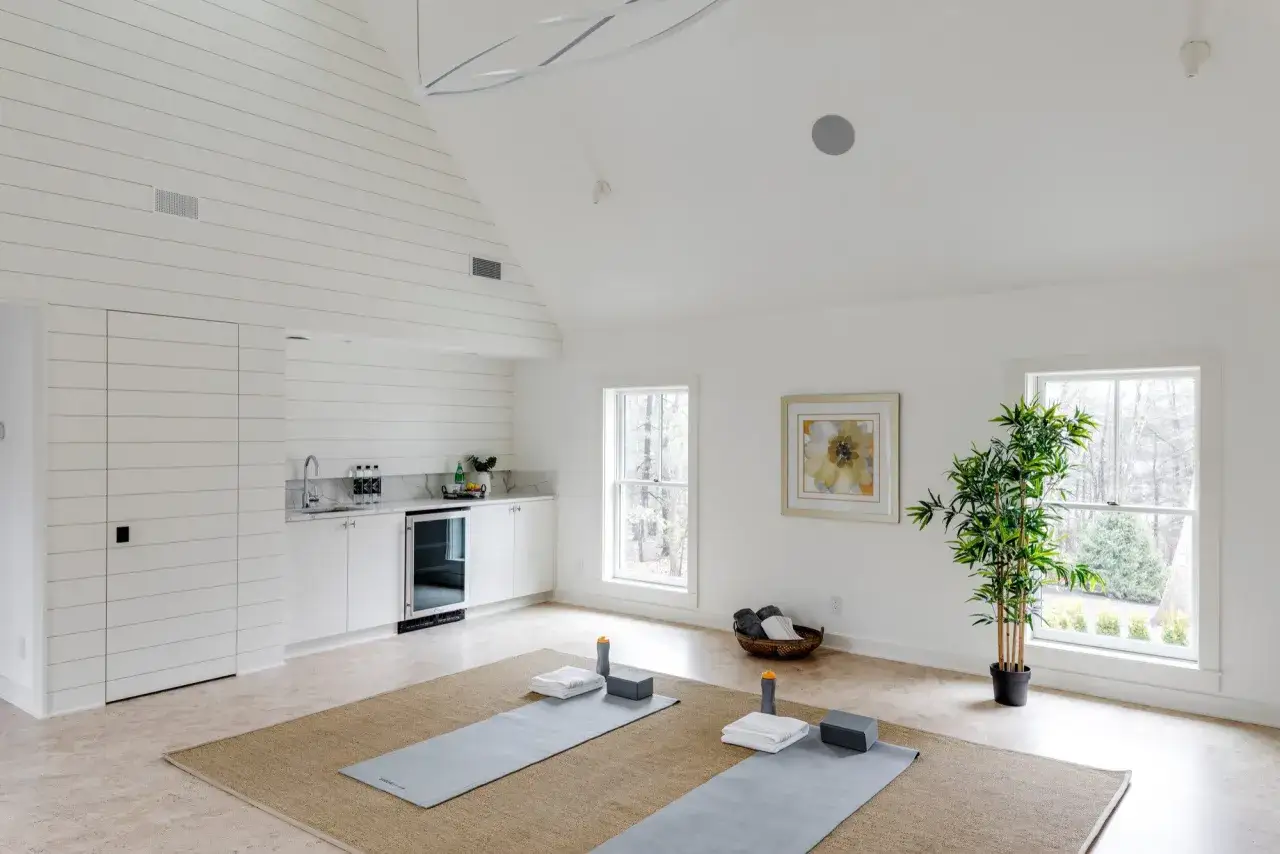 Ett ljust och luftigt yogarum hemma med två yogamattor, klossar, handdukar och en bambuplanta. Ett litet pentry finns i bakgrunden.