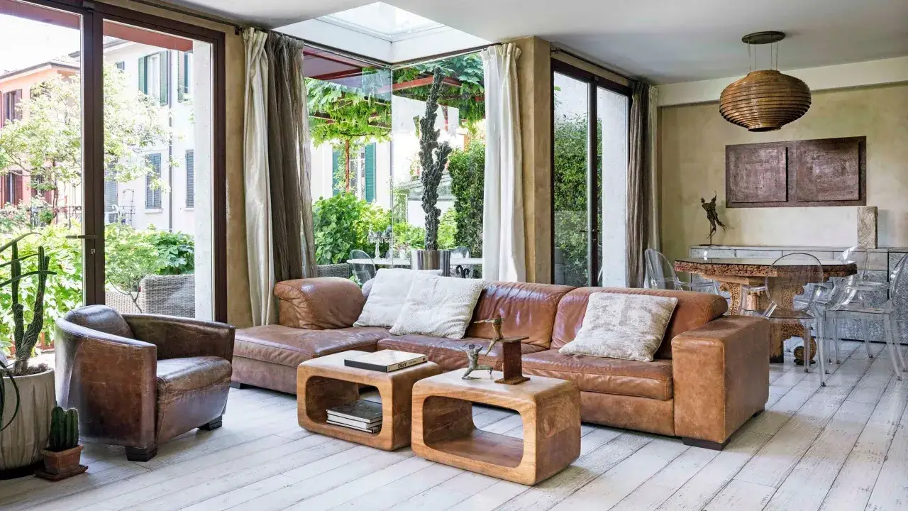 Accogliente soggiorno etnico chic con divano in pelle, poltrona vintage e vista sul giardino.