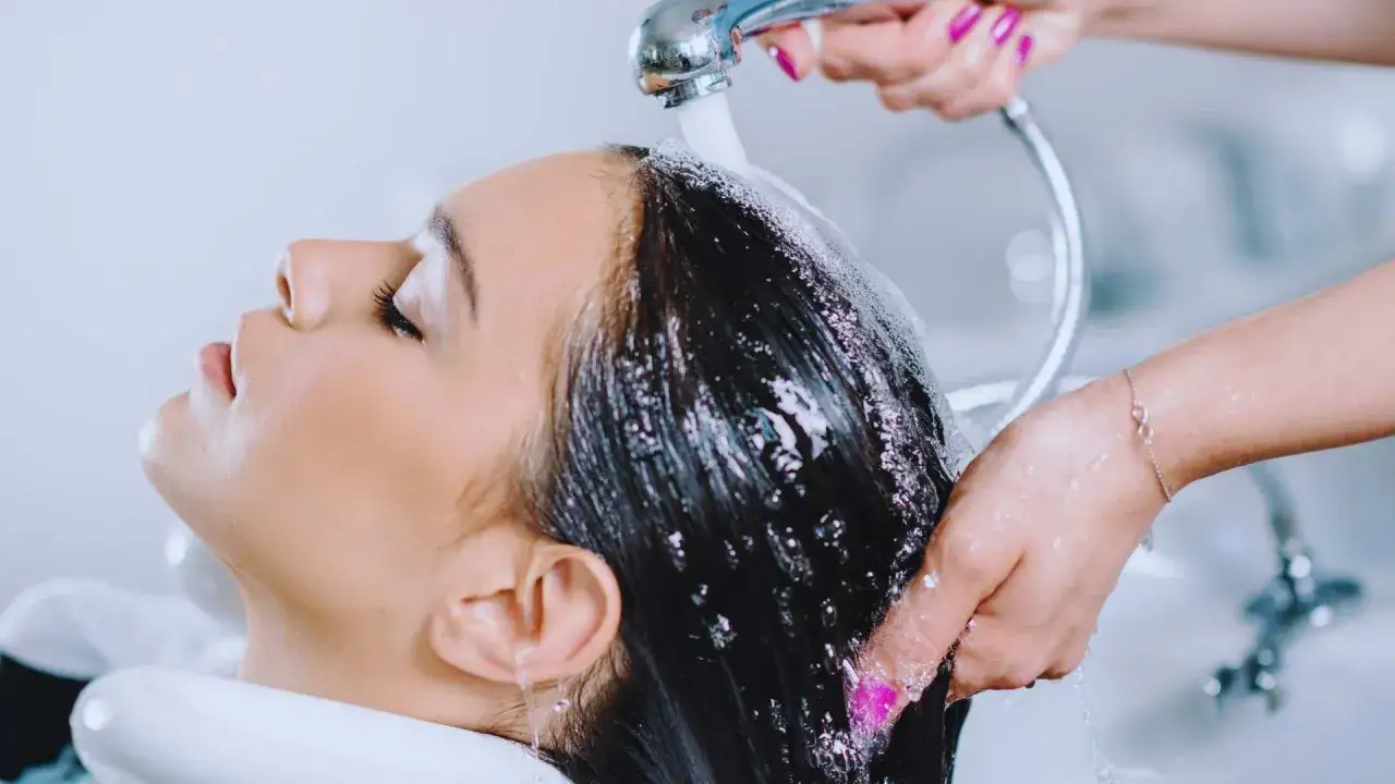 Una peluquera lava el cabello de una clienta, preparándolo para cortar el pelo en seco o mojado.