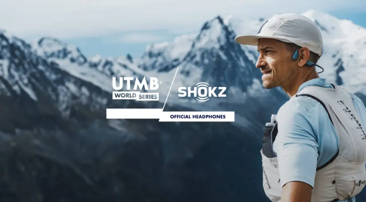 Un coureur UTMB World Series, équipé d'écouteurs Shokz, profite du podcast trail avec un panorama de montagnes enneigées.