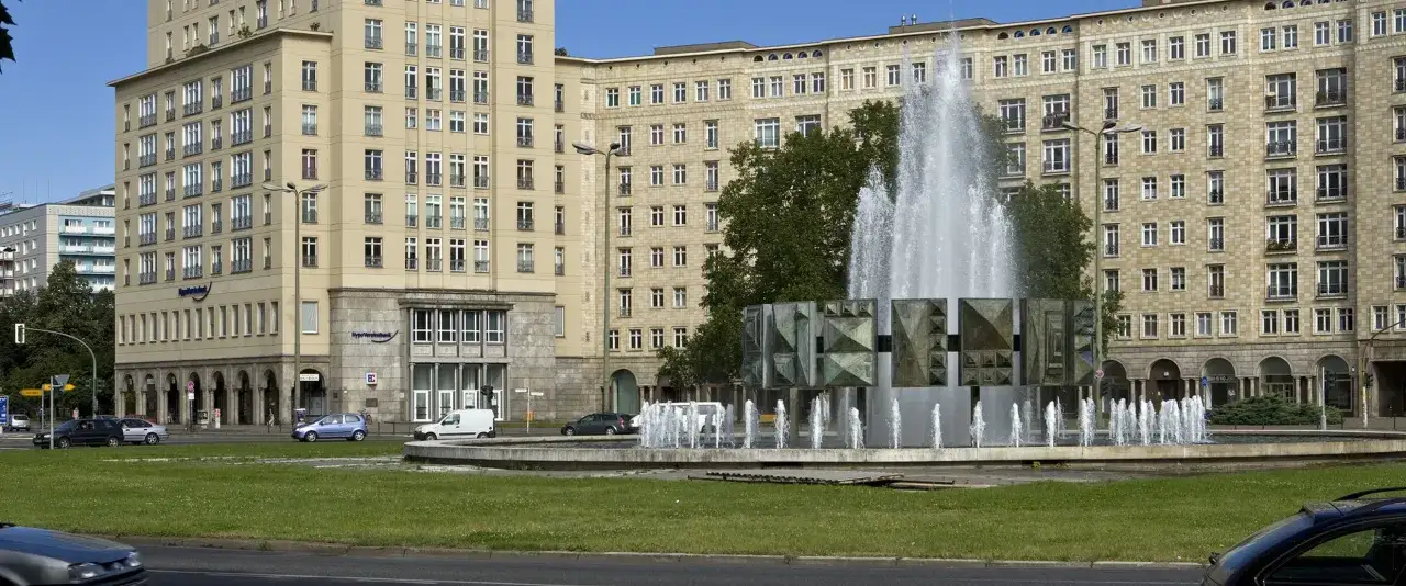Brunnen auf der Stalinallee Berlin, flankiert von monumentalen Geb&auml;uden mit vielen Fenstern.