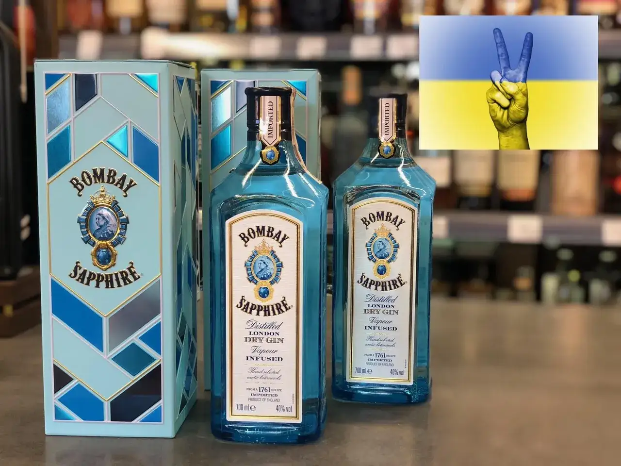 Dwie butelki Bombay Sapphire, popularnego alkoholu, obok pudełka. W tle flaga Ukrainy z symbolem pokoju.