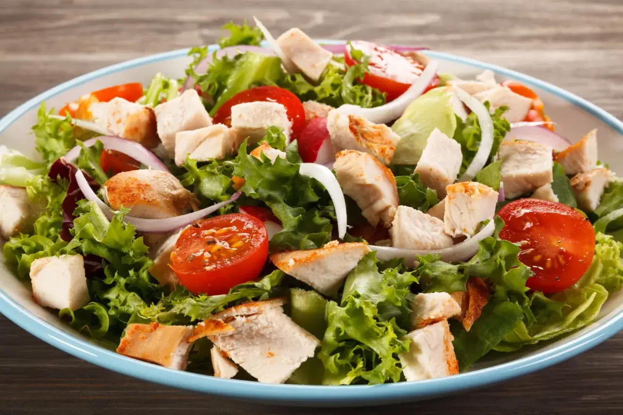 Insalata di pollo fresca e colorata con lattuga, pomodorini, cipolla rossa e pezzi di pollo grigliato.
