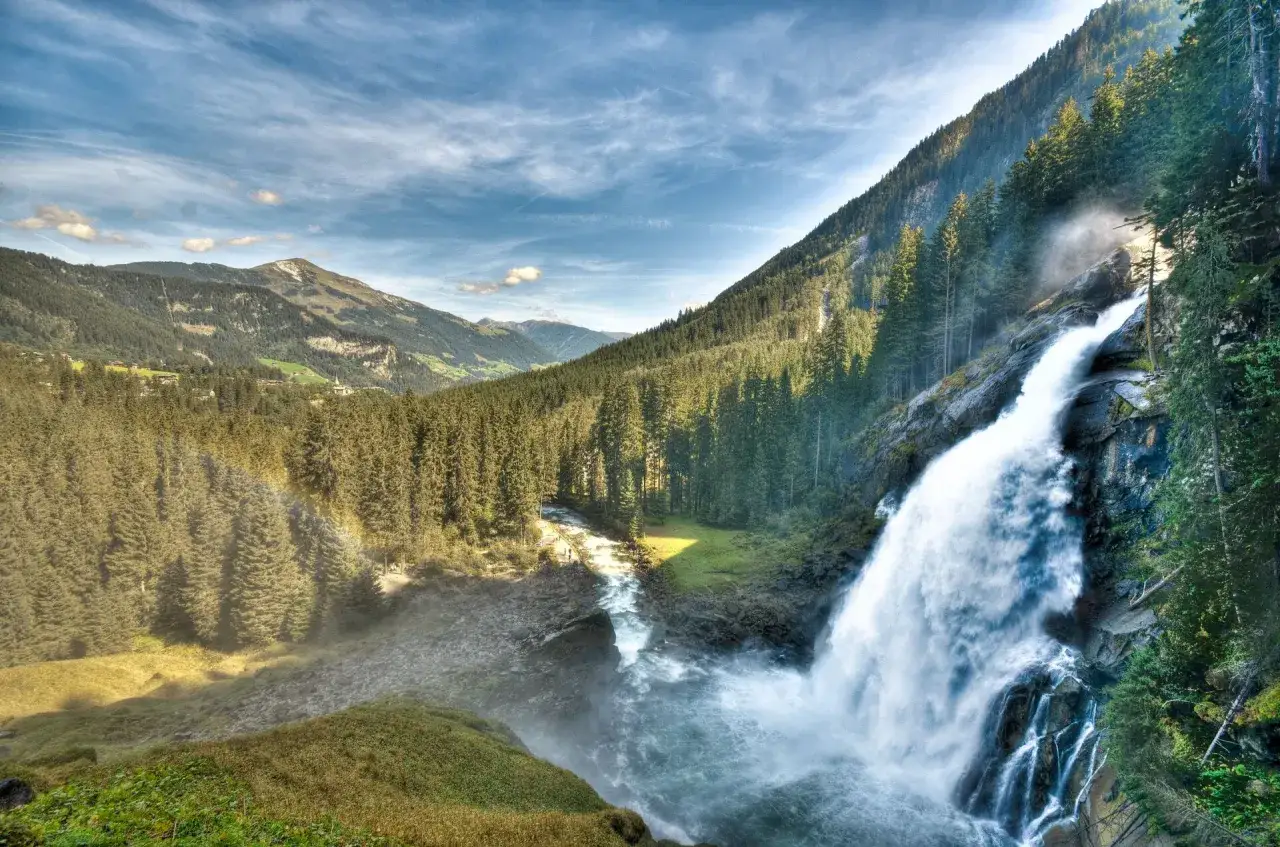 Majest&auml;tischer zell am see wasserfall st&uuml;rzt in ein rauschendes Becken, umgeben von dichten W&auml;ldern und Bergen. Ein Regenbogen tanzt im Spr&uuml;hnebel.