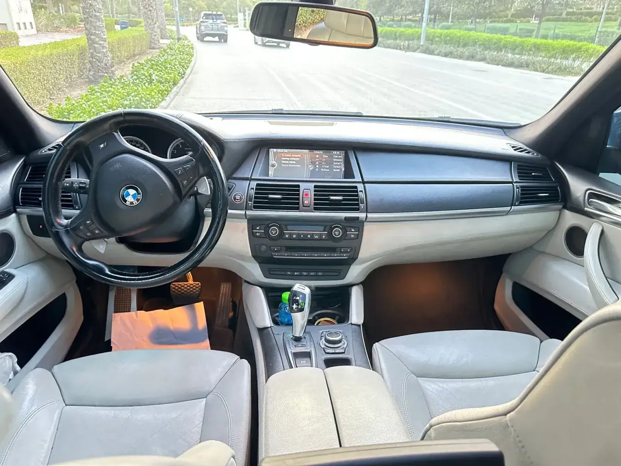 Wnętrze BMW X5 E70 z jasną tapicerką i czarną kierownicą. Widok na drogę i inne samochody.