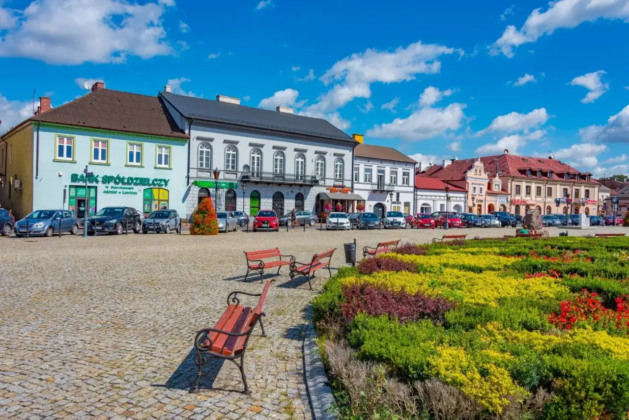 Kolorowy rynek z kwitnącymi rabatami, ławkami i kamienicami. Idealne miejsce na tani city break.