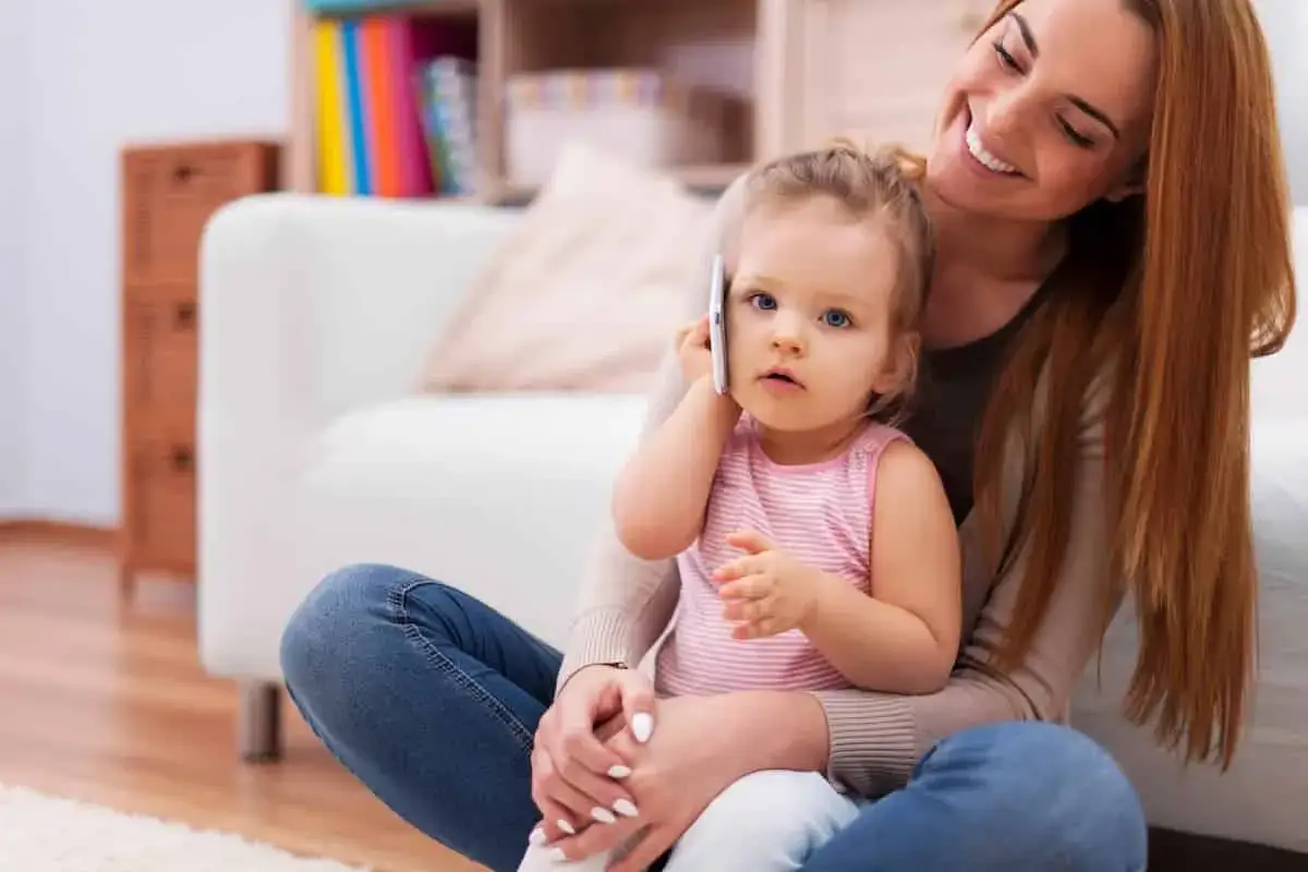 Mam&aacute; sonr&iacute;e mientras su beb&eacute;, con su tel&eacute;fono m&oacute;vil, practica sus primeras palabras.