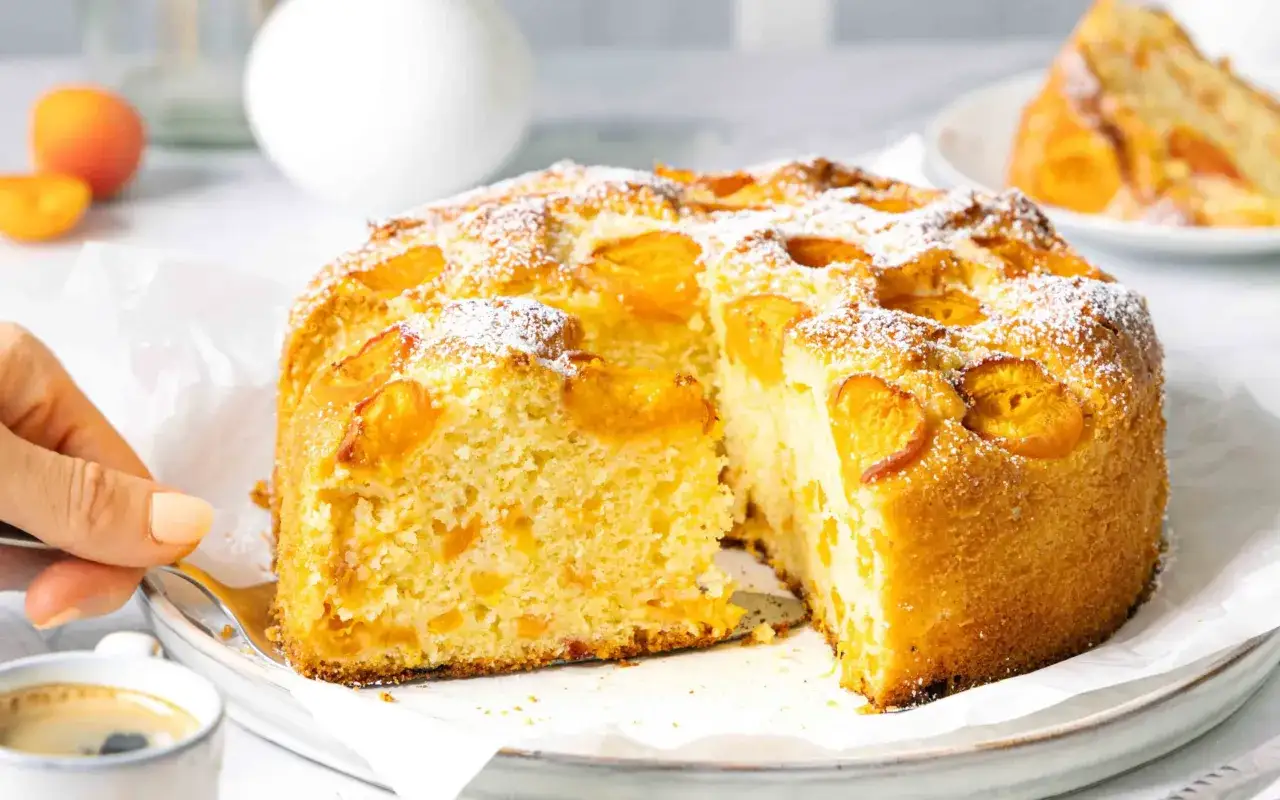 Ein saftiger aprikosenkuchen mit frischen aprikosen, bestäubt mit Puderzucker. Eine Gabel wird angesetzt, um ein Stück zu entnehmen.