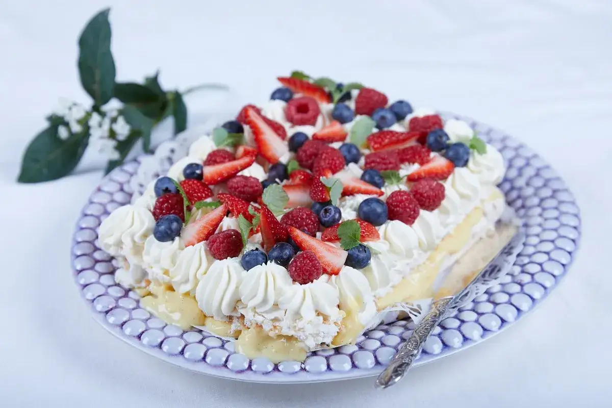 En hjärtformad pavlova med vispgrädde, vaniljkräm och massor av färska jordgubbar och bär.