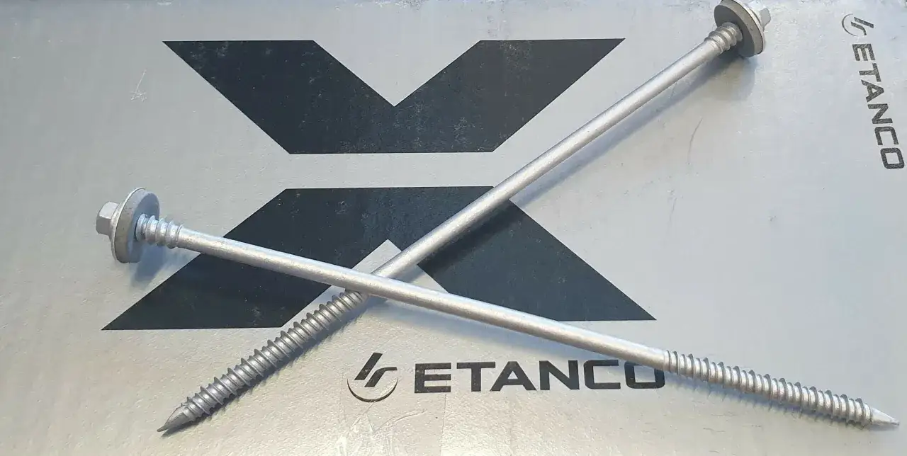 Dwa metalowe śrubki z podkładkami, leżące na szarej powierzchni z logo ETANCO.