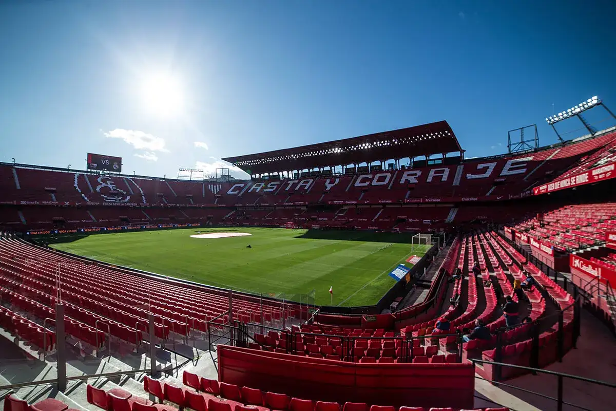 Puste trybuny stadionu Ram&oacute;n S&aacute;nchez Pizju&aacute;n przed meczem Sevilla FC. Słońce świeci nad boiskiem, zapowiadając emocjonujące rozgrywki.