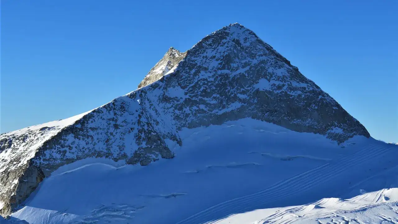Der Olperer Nordgrat ragt schneebedeckt in den blauen Himmel. Spuren im Schnee deuten auf eine beliebte Route hin.