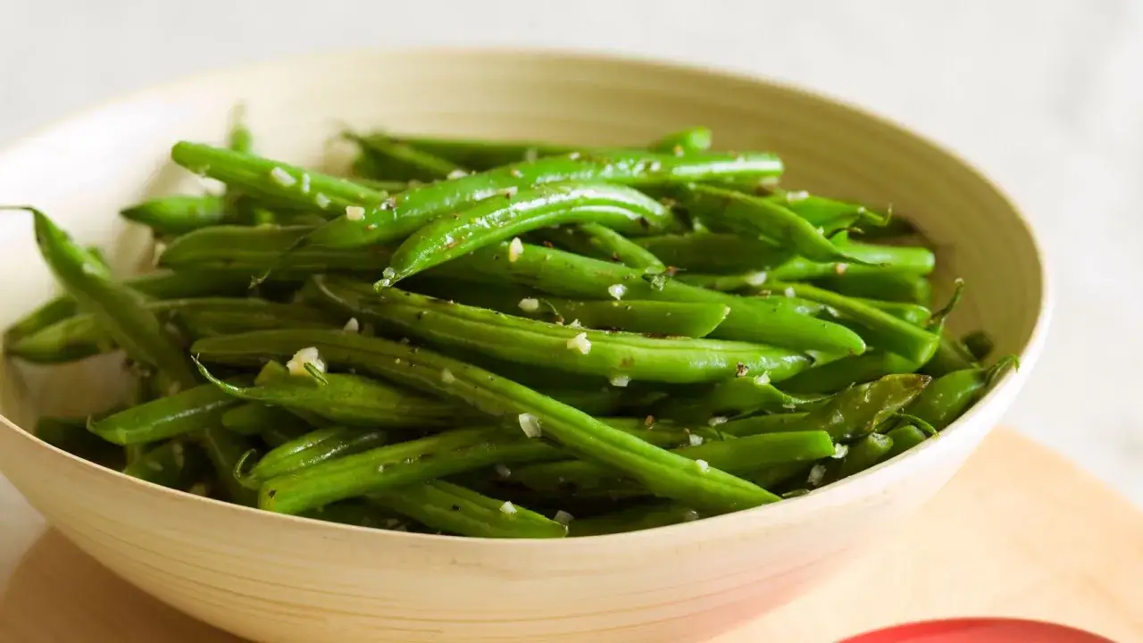 Fagiolini in padella, conditi con aglio e pepe, serviti in una ciotola di legno.