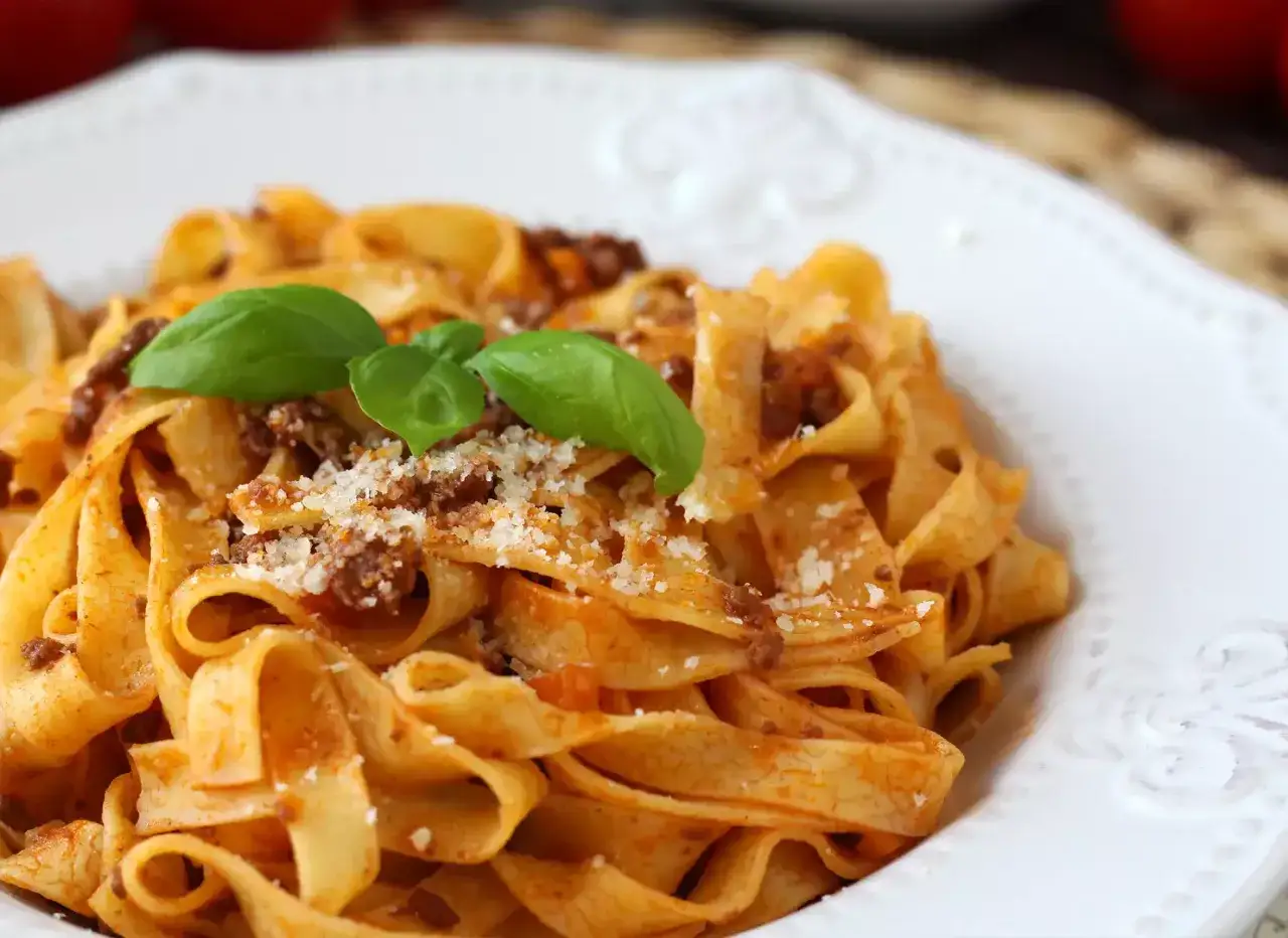 Fettuccine con abundante salsa boloñesa, espolvoreado con queso rallado y decorado con hojas de albahaca fresca.