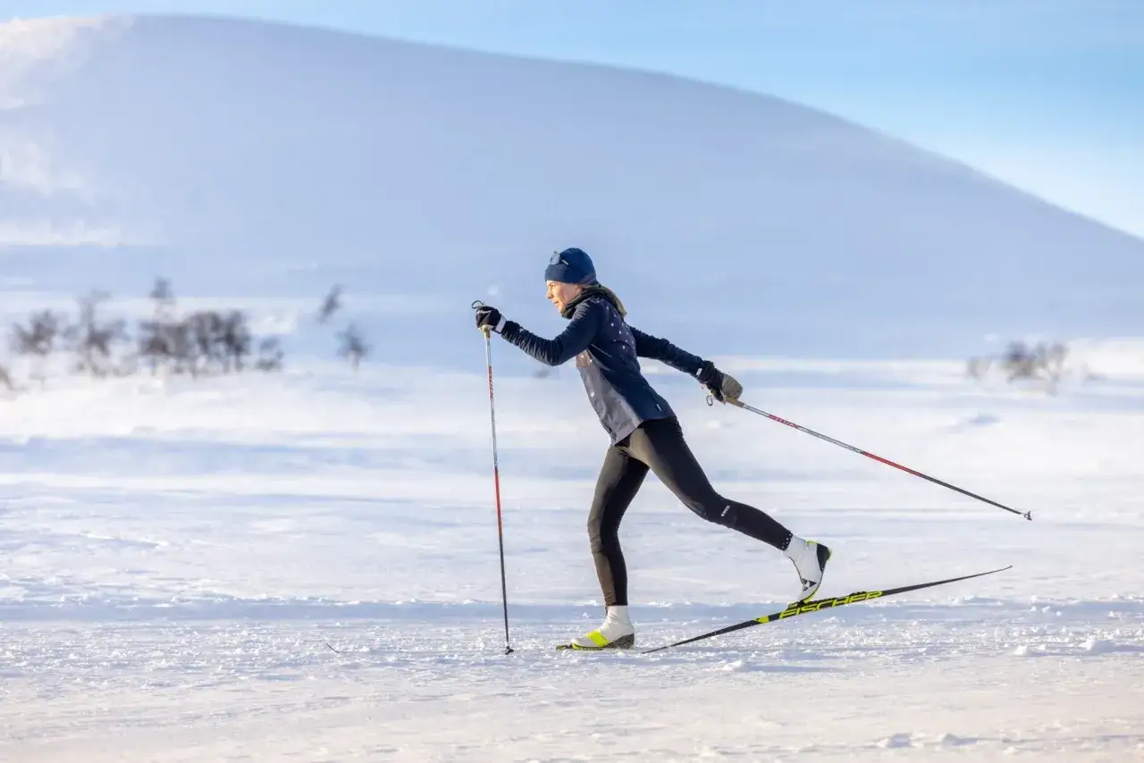 En kvinna åker längdskidor i ett snöigt landskap. Hon använder stavar och skidor, och visar upp en av de olika skidstilarna.