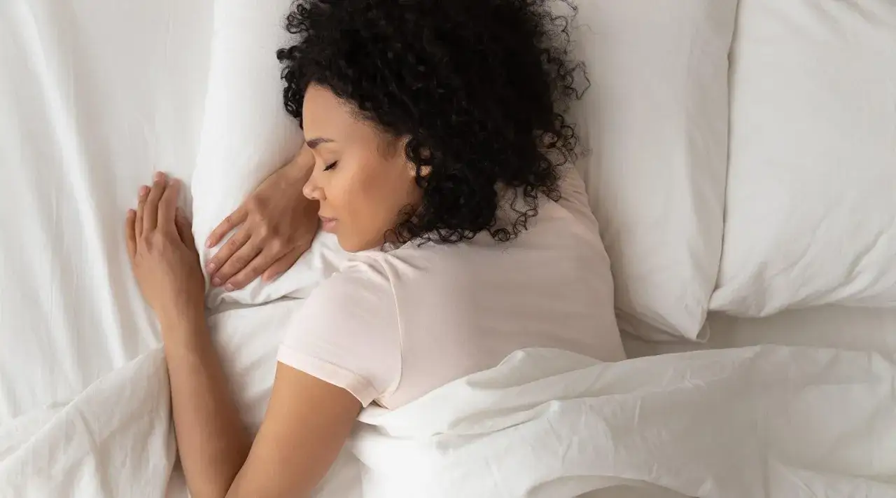 Frau schl&auml;ft friedlich auf einem wei&szlig;en Bett. Sie liegt auf der Seite, die Arme unter dem Kopf. Vielleicht sucht sie nach einer bequemen Position, wie schlafen mit tennisarm.