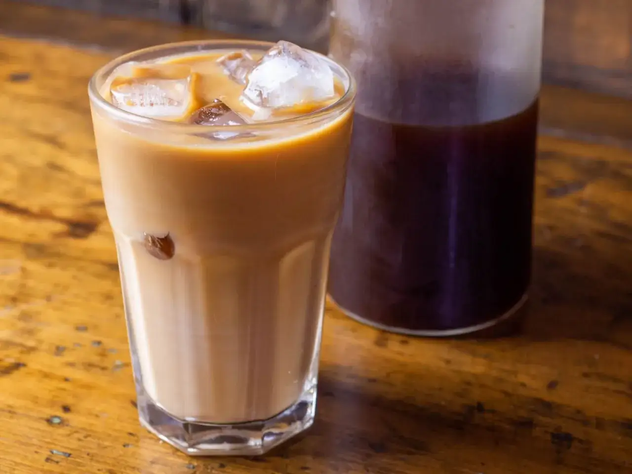 Erfrischender kalter Kaffee mit Eiswürfeln in einem Glas, daneben eine Karaffe mit dunklem Kaffee. Perfekt für heiße Tage!