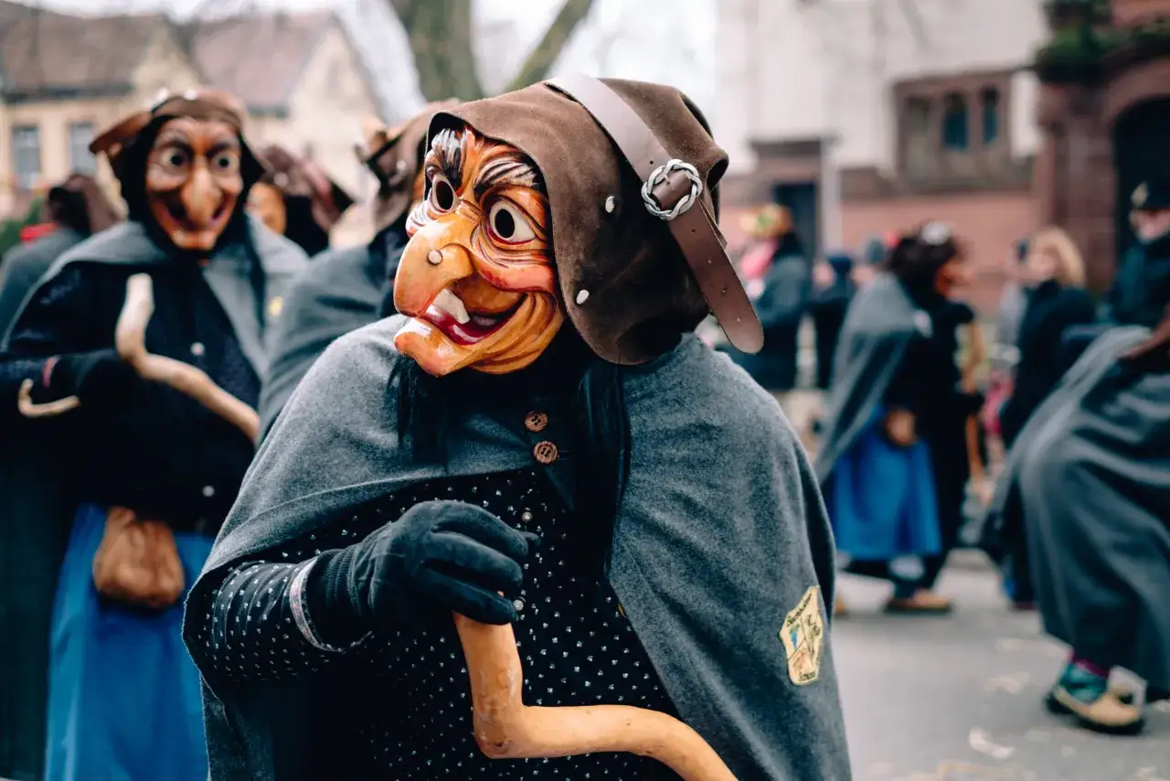 Maschere di befane belle e spaventose sfilano in parata, con cappelli marroni e mantelli grigi.