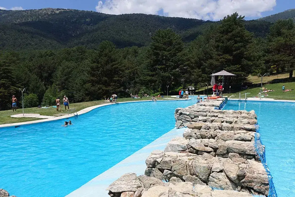Gente disfrutando del sol y el agua en el embalse de Navalmedio, rodeado de pinos y monta&ntilde;as.