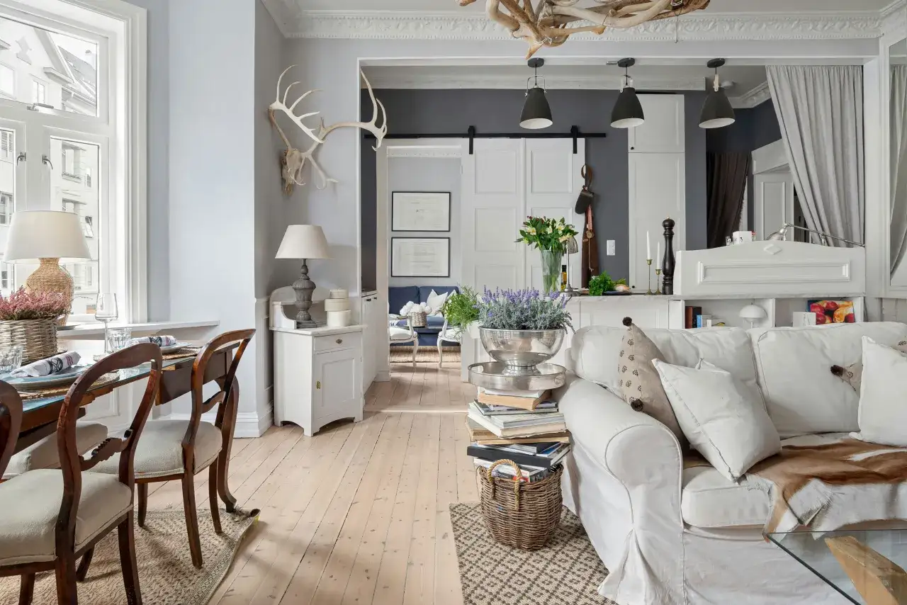 Un salotto con un'atmosfera da arredamento francese chic. Tavolo da pranzo in legno, divano bianco accogliente, lampade e decorazioni uniche.
