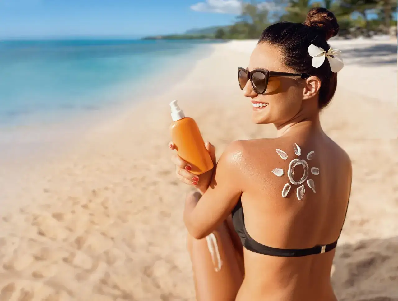 Donna con pelle abbronzata sulla spiaggia, applica crema solare a forma di sole sulla schiena.