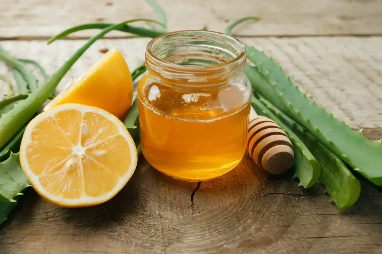 Un pot de miel doré, des citrons frais et des feuilles d'aloe vera sur fond de bois. Un remède de grand-mère contre les rides, naturel et efficace.