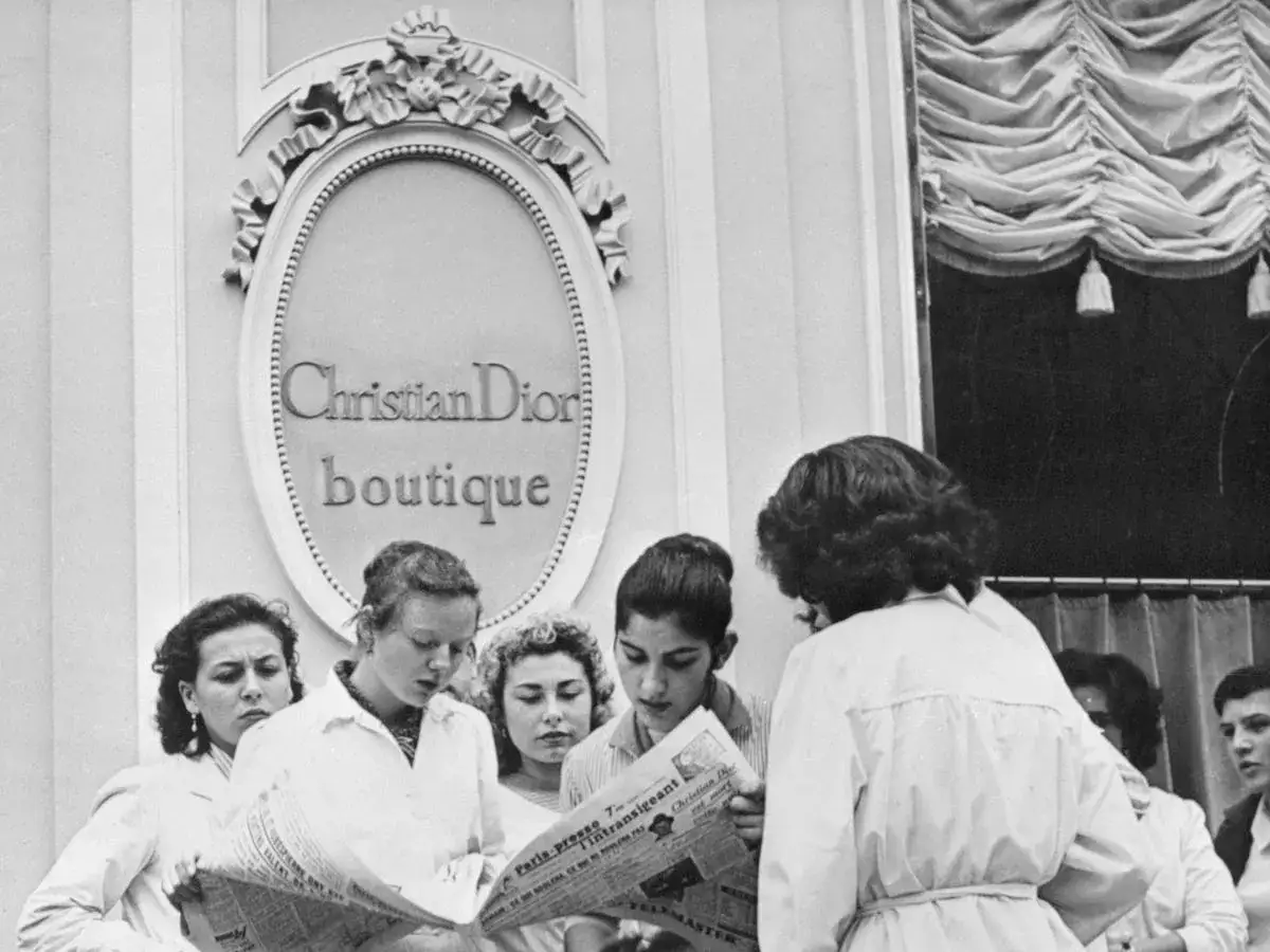 Donne leggono un giornale davanti alla boutique Christian Dior, simbolo dell'eleganza francese.