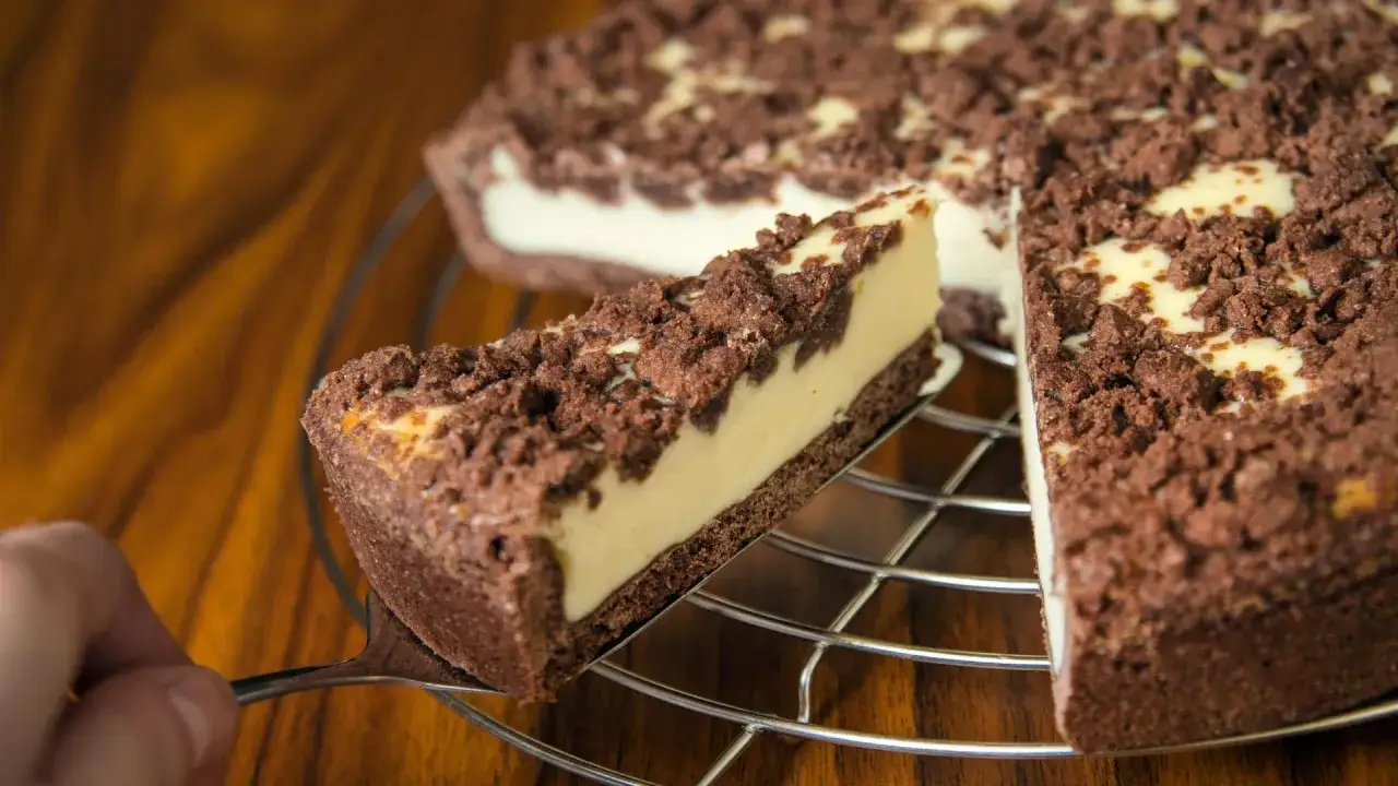 Ein St&uuml;ck russischer Zupfkuchen wird aus dem Ganzen gehoben. Der Kuchen hat einen dunklen Boden, eine helle F&uuml;llung und eine kr&uuml;melige Schokoladenstreusel-Decke.